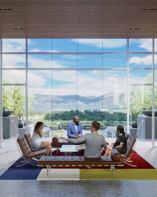 A group of people sit and converse in a modern, open space with large windows offering a scenic view of mountains and greenery.