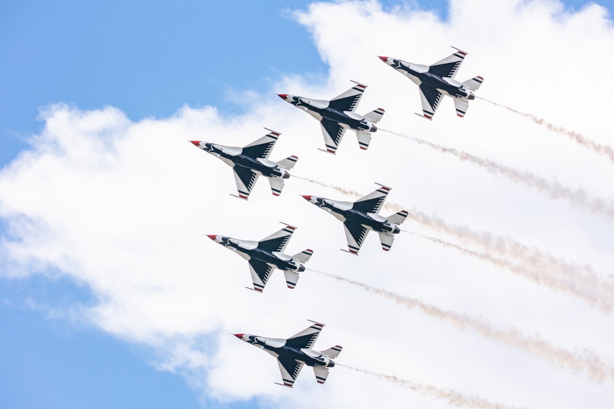 Six fighter jets flying in formation against a cloudy sky, leaving smoke trails in their wake.