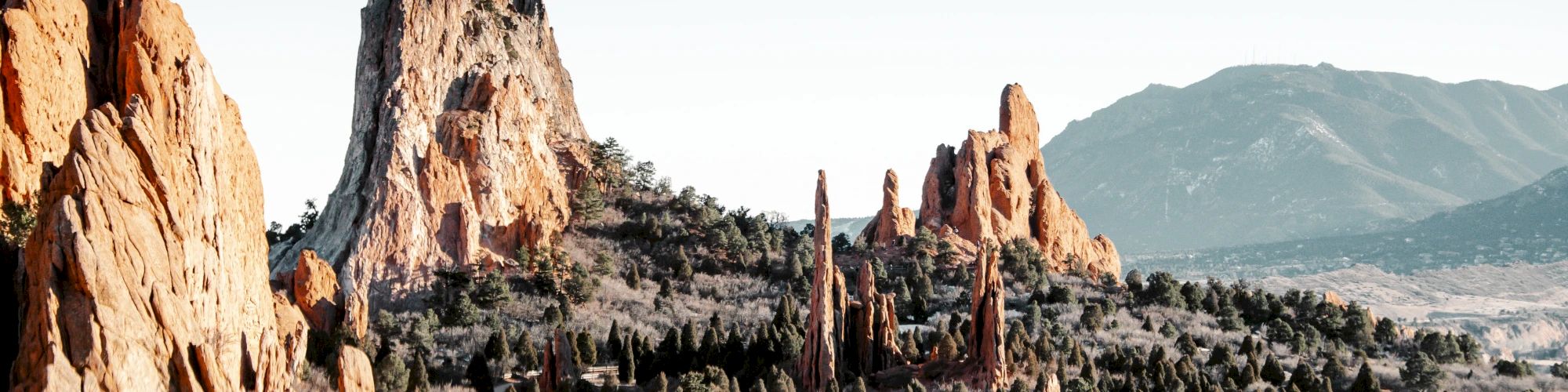 The image shows a landscape with dramatic rock formations, sparse vegetation, and distant mountains under a clear sky.