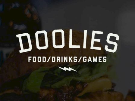 An image showing the text "DOOLIES FOOD/DRINKS/GAMES" with a background suggesting food items.