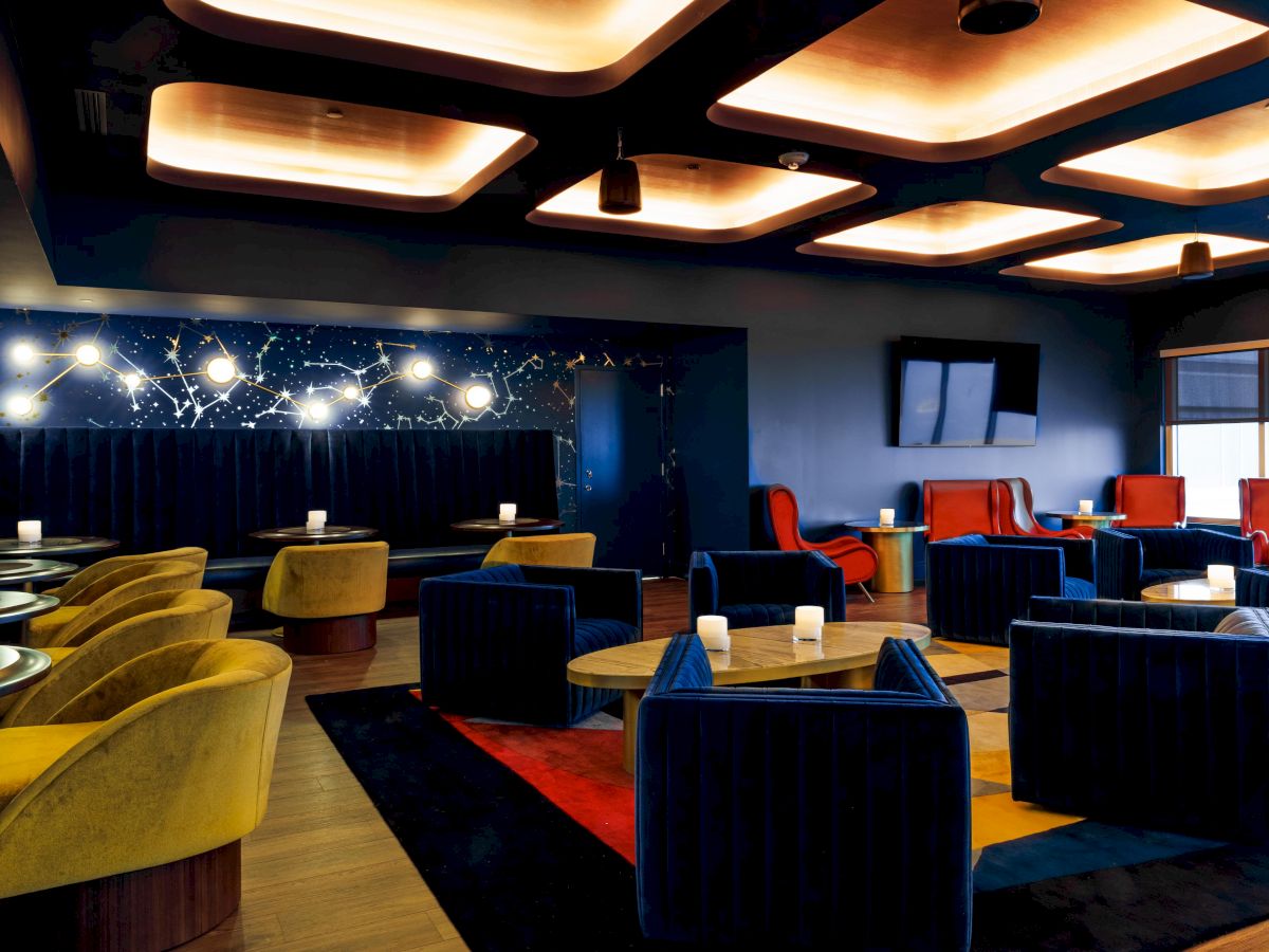 A stylish lounge with colorful chairs, modern lighting, and a cozy atmosphere is depicted in the image.