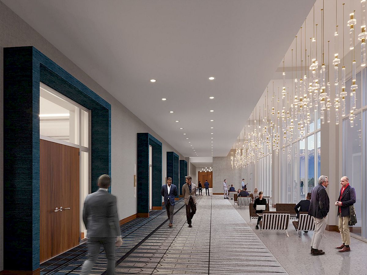 This image features a modern hallway with people walking and interacting, elegant lighting fixtures, large windows, and a seating area.