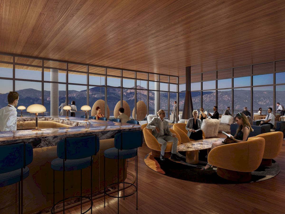 The image shows a modern, upscale lounge with people socializing, a bar area with high chairs, and large windows offering a scenic view of mountains.