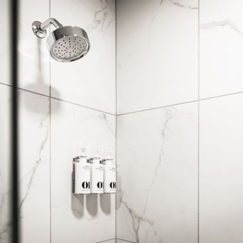 A bathroom shower area with a showerhead, handheld shower, and wall-mounted dispensers on marble tiles.