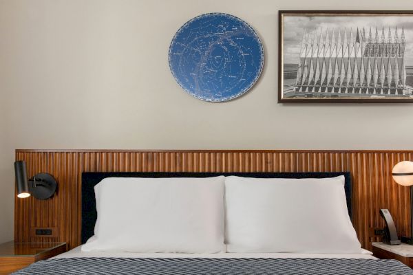 A neatly made bed with white pillows and a blue patterned blanket is centered below a decorative circular piece and a framed artwork.