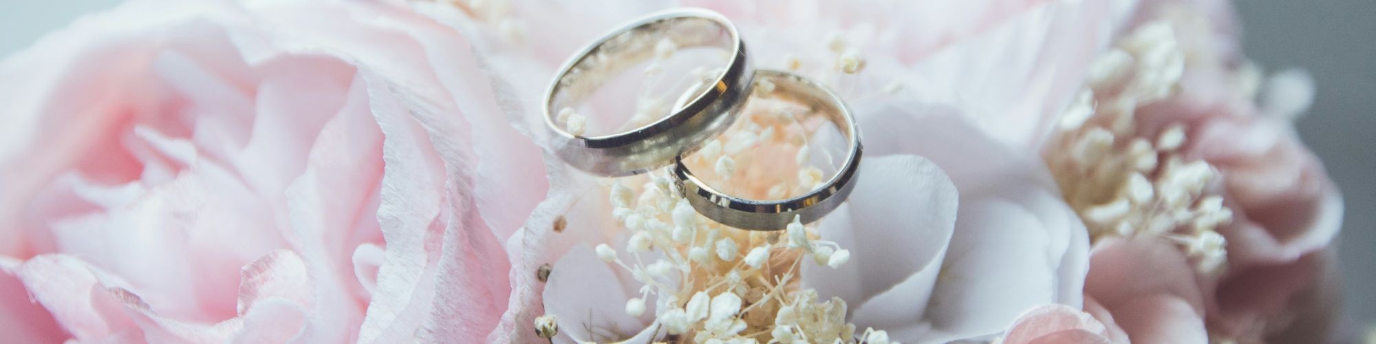 The image shows two wedding rings placed on a bouquet of pastel-colored flowers, including pink roses and baby's breath.