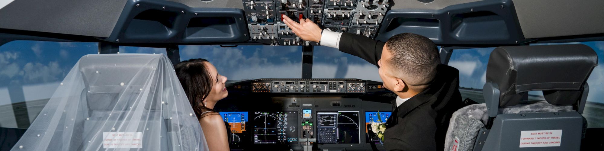 A couple in wedding attire is in an airplane cockpit simulator, interacting with the controls.