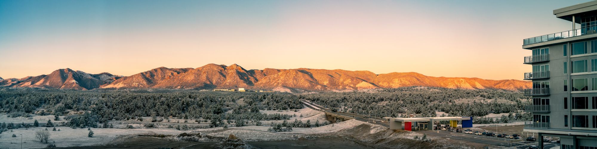 A scenic view of snow-dusted mountains at sunrise, with a building on the right and a road leading through the snowy landscape.