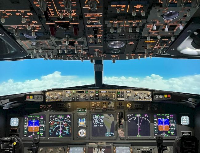 This image shows the cockpit of an aircraft, with various control panels, switches, and displays, and a view of the blue sky and clouds outside.