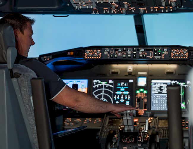 A pilot operating an aircraft cockpit, surrounded by various controls, screens, and instruments, indicating active flight operations.