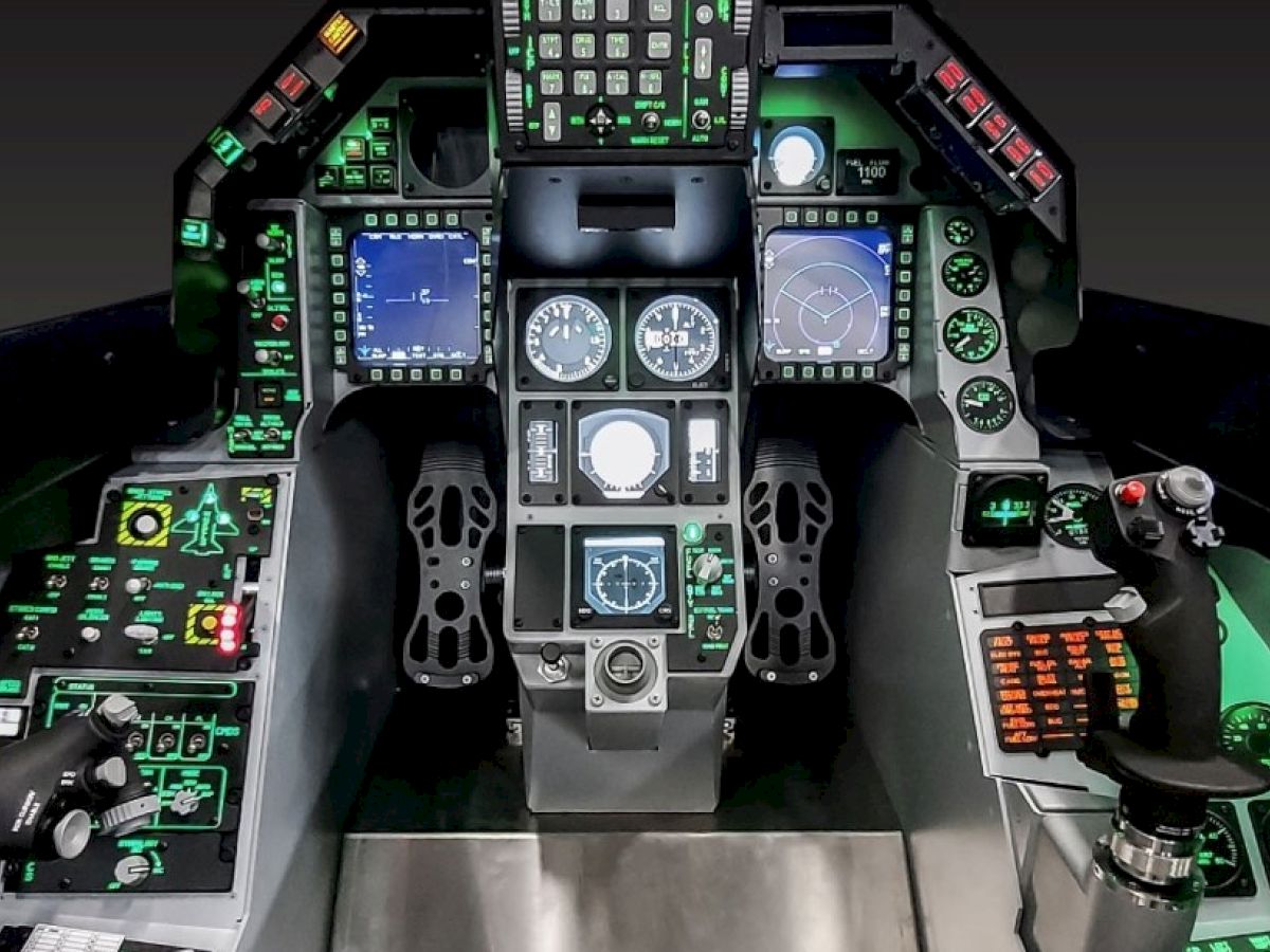 The image shows the cockpit of a fighter jet, featuring various controls, displays, and instruments with illuminated buttons and screens.