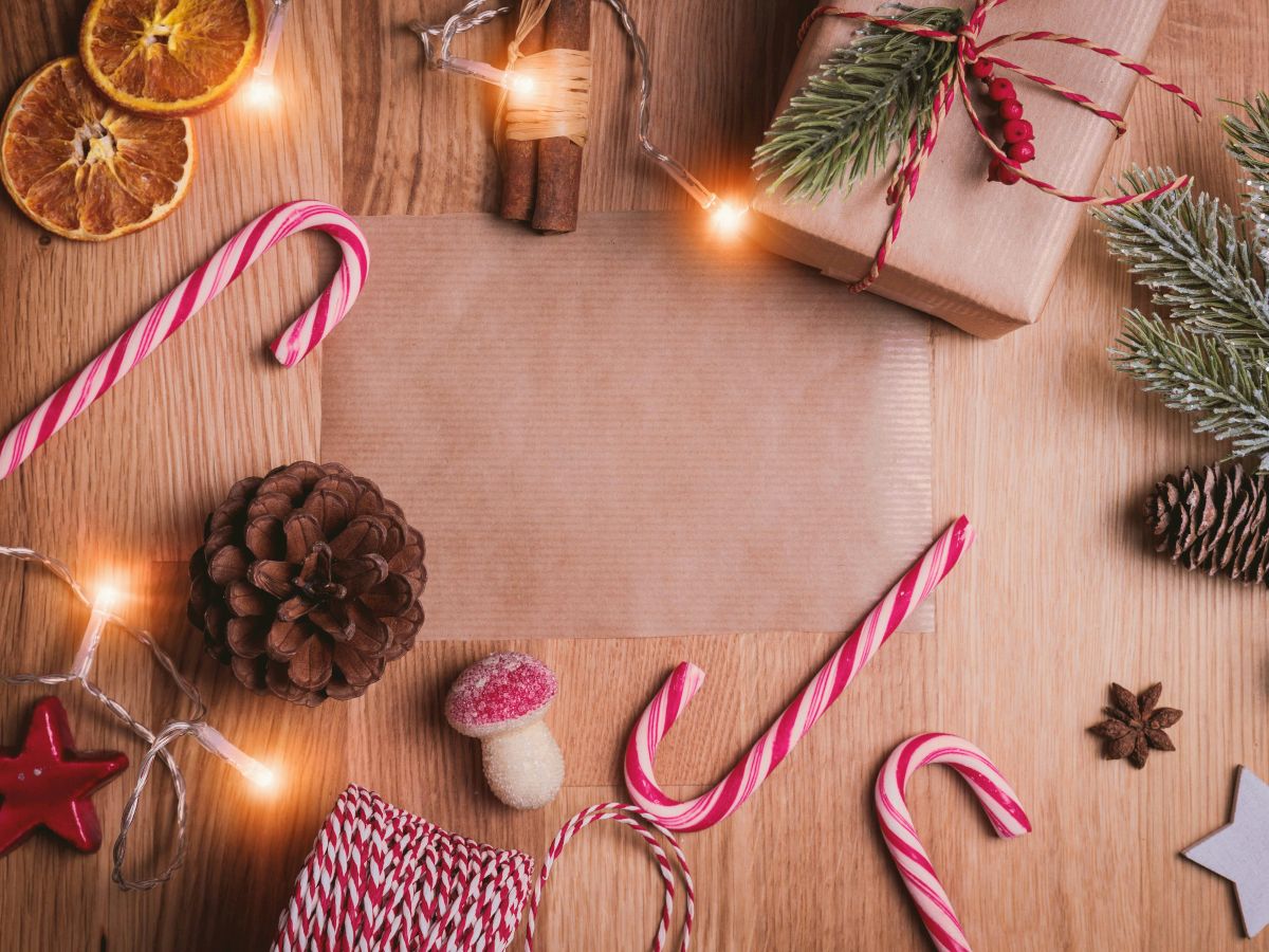 The image features Christmas decorations: candy canes, pine cones, dried orange slices, lights, and wrapped gifts on a wooden surface.