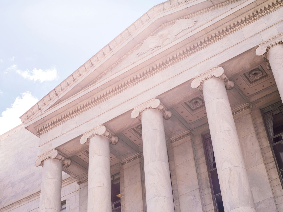 A classical building facade with tall columns and decorative elements, under a partly cloudy sky.