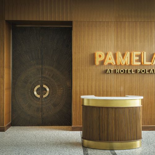 A wooden reception desk is in front of a wall with the illuminated sign 