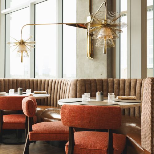 A stylish restaurant interior with orange chairs, round tables, and unique lighting is showcased in the image.