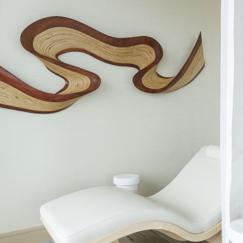 A modern lounge area with a white chaise lounge, abstract wood wall art, and light decor.