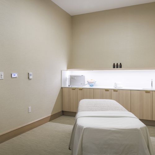 A minimalist spa room with a massage table, wooden cabinets, and a softly lit atmosphere, creating a calming space.