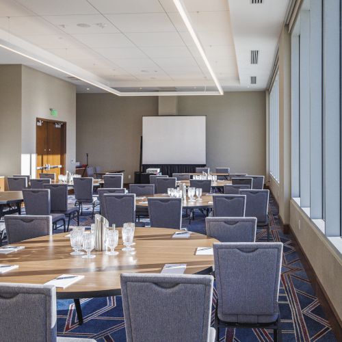 A modern conference room with chairs, tables, and a projector screen, set up for a meeting or presentation.