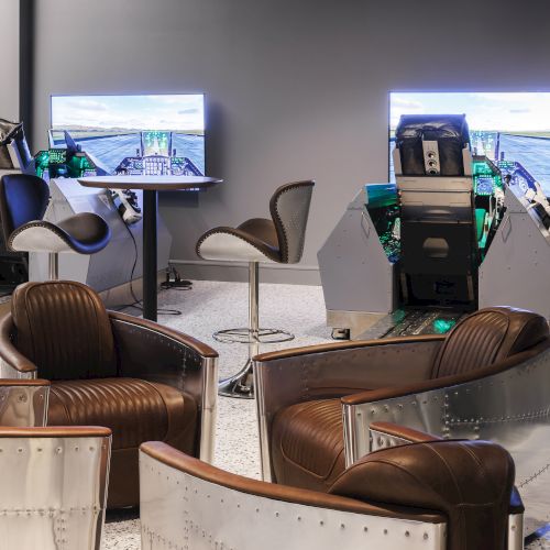 The image shows a room with racing simulators, modern seating, and screens displaying driving simulations.