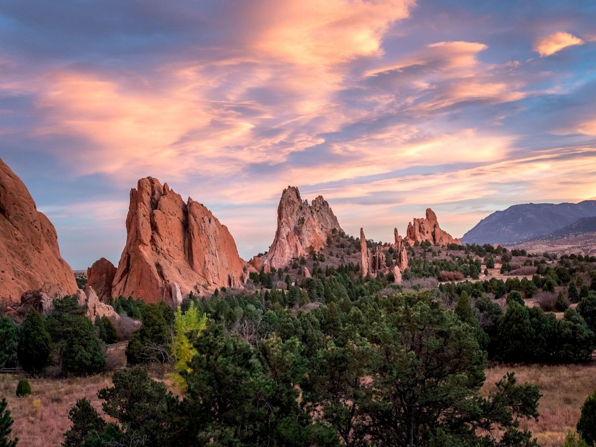 A stunning landscape with rocky formations, evergreen trees, and a vibrant sky with colorful clouds at sunset.