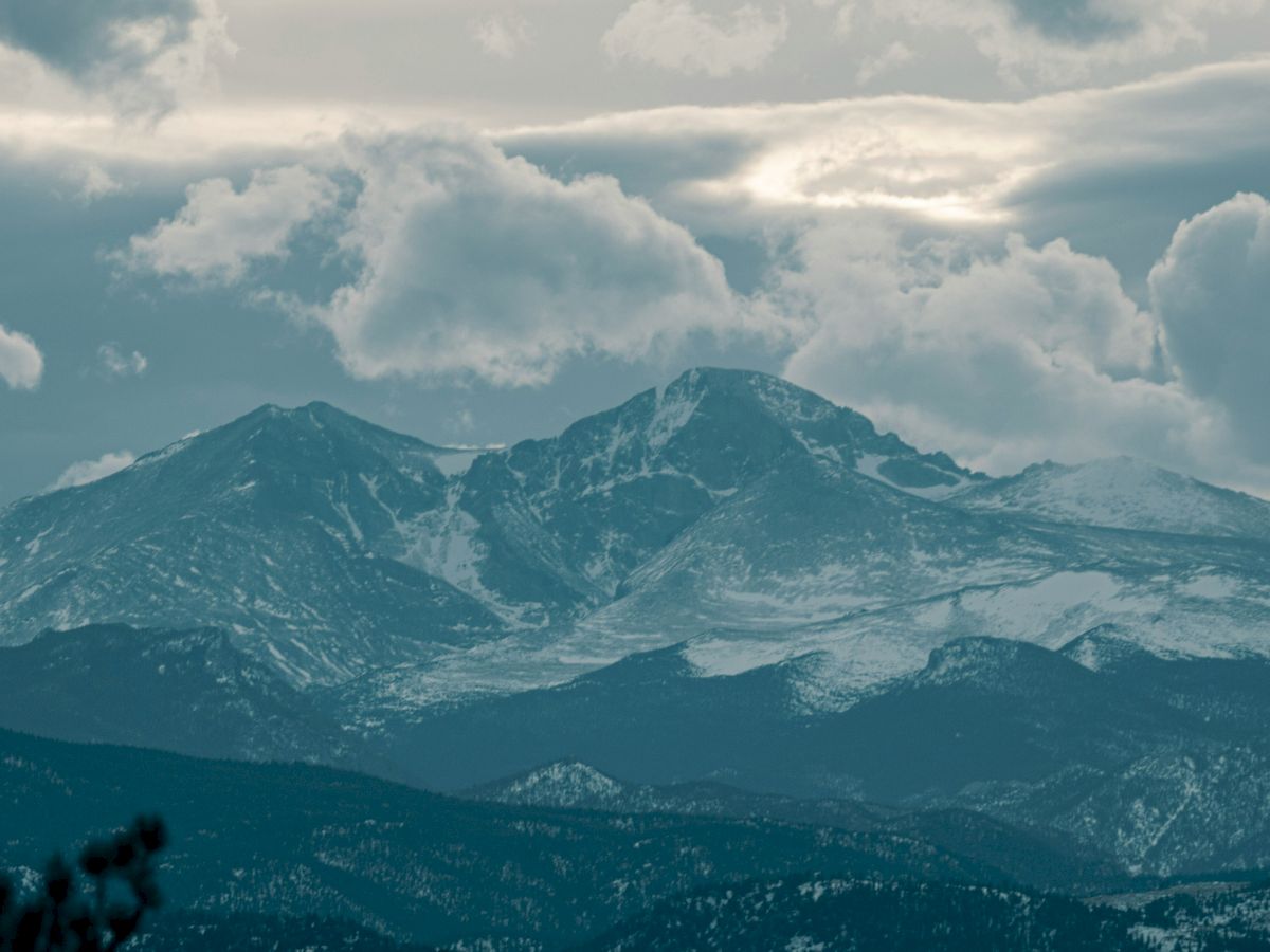 A scenic image of a mountainous landscape with snow-capped peaks surrounded by clouds and a dramatic sky.