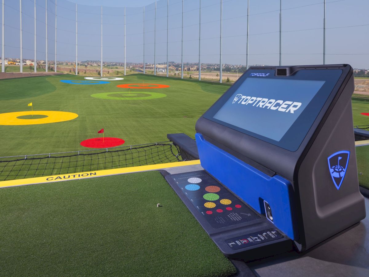 A driving range with colorful targets on the grass and a touchscreen interface of a Toptracer system in the foreground.