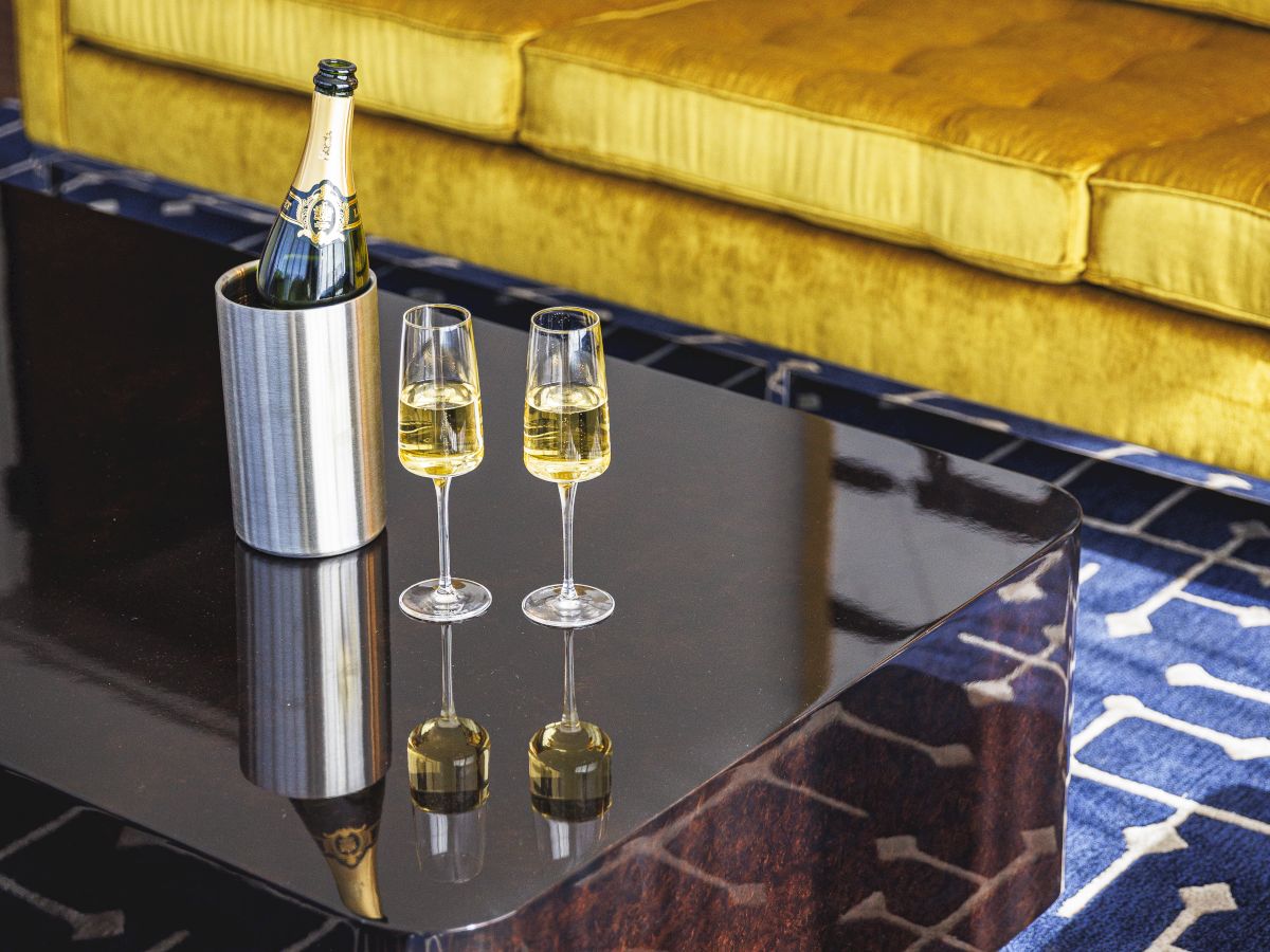 A yellow couch, a modern coffee table with a champagne bottle in an ice bucket, and two filled glasses on a blue patterned rug.