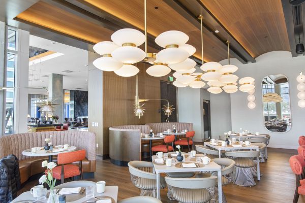 A modern restaurant interior with round tables, elegant seating, chic lighting fixtures, and decorative mirrors on the walls.