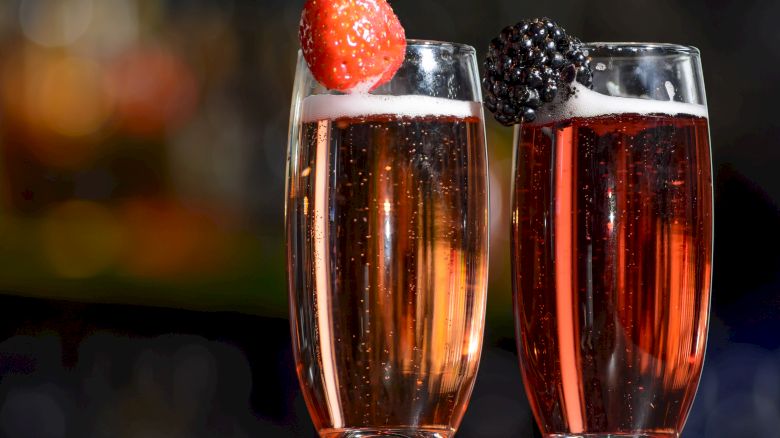 Two champagne flutes filled with a red sparkling beverage, each garnished with a strawberry and a blackberry.