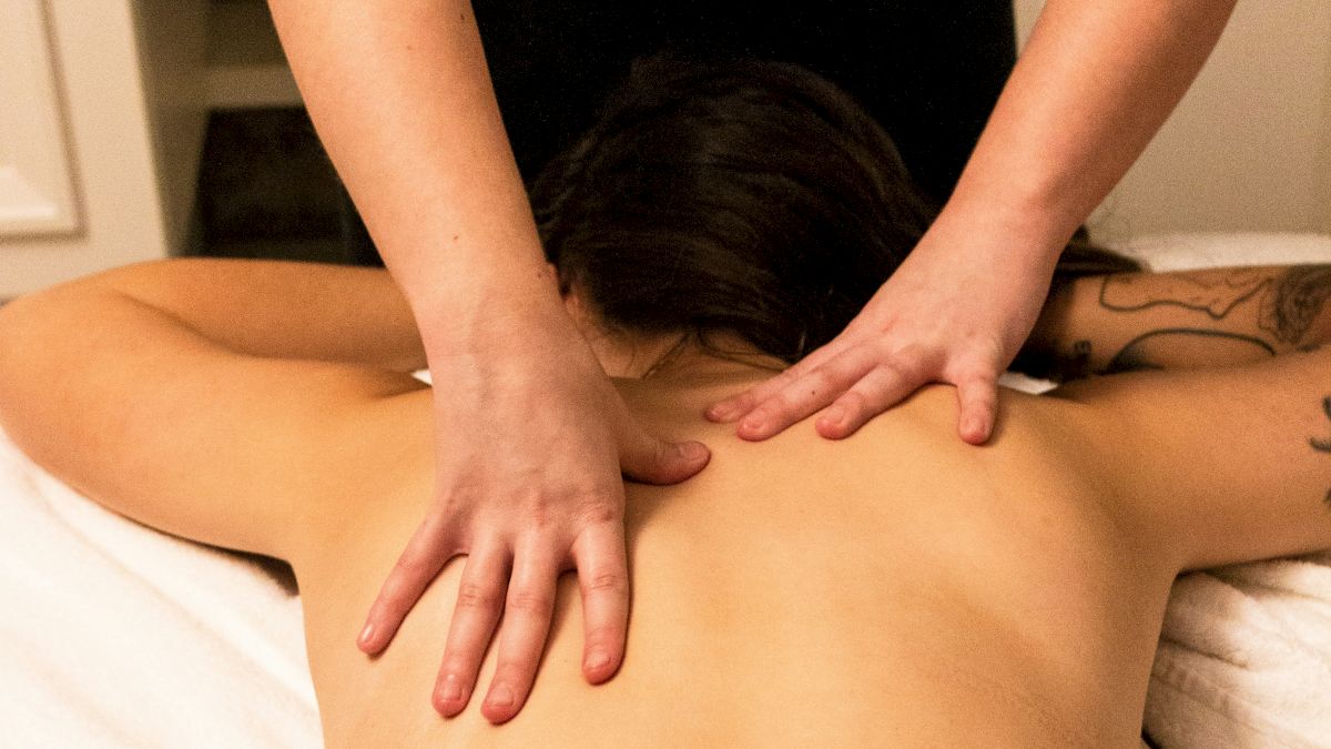 A person receiving a back massage, lying face down on a table with a white towel covering the lower body.
