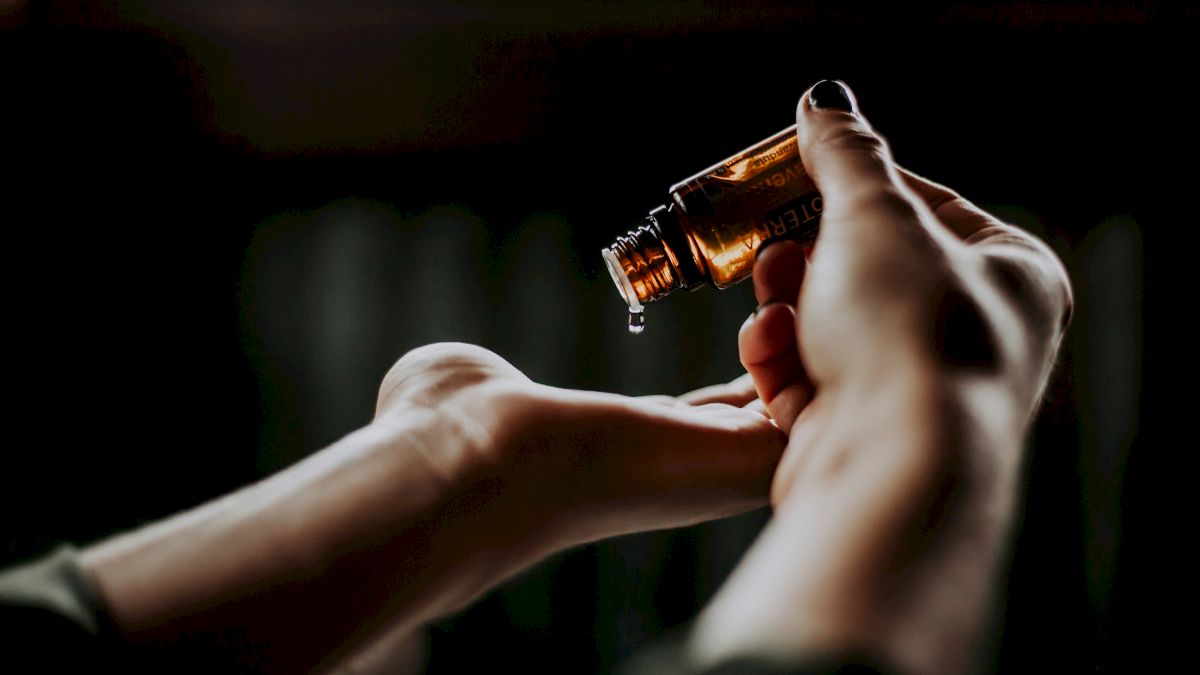 A person is pouring liquid from a small amber bottle onto their open palm.