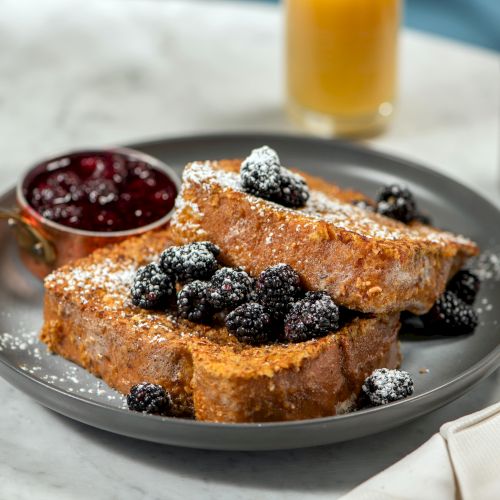 The image shows French toast with blackberries and powdered sugar, accompanied by a small container of berry sauce on a plate.