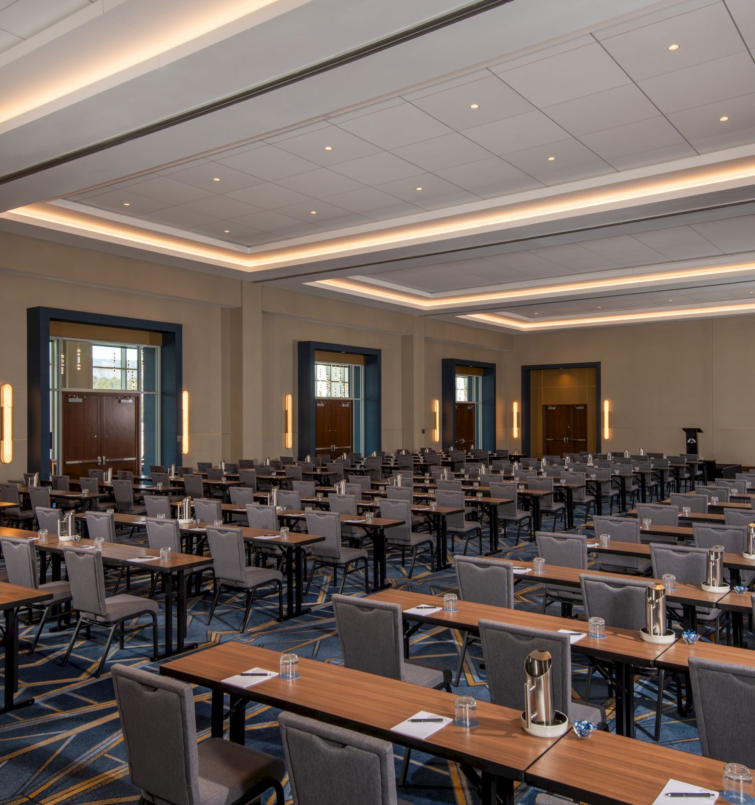 The image shows a large conference room set up with rows of tables and chairs, water pitchers, and notepads, ready for a meeting or event.