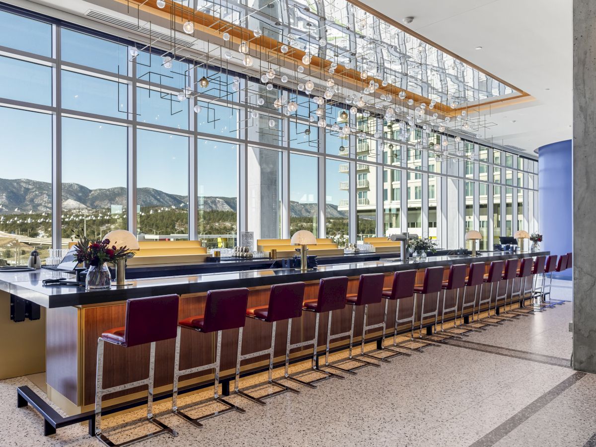 A modern bar with red stools, a sleek countertop, large windows offering mountain views, and stylish lighting above.