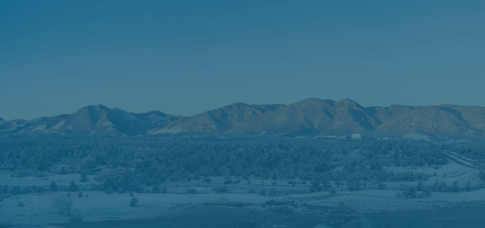 A snow-covered landscape with a range of mountains under a clear blue sky.