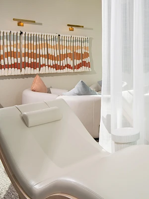 The image features a spa-like setting with white lounge chairs, sheer curtains, and minimalistic decor, creating a relaxing atmosphere.
